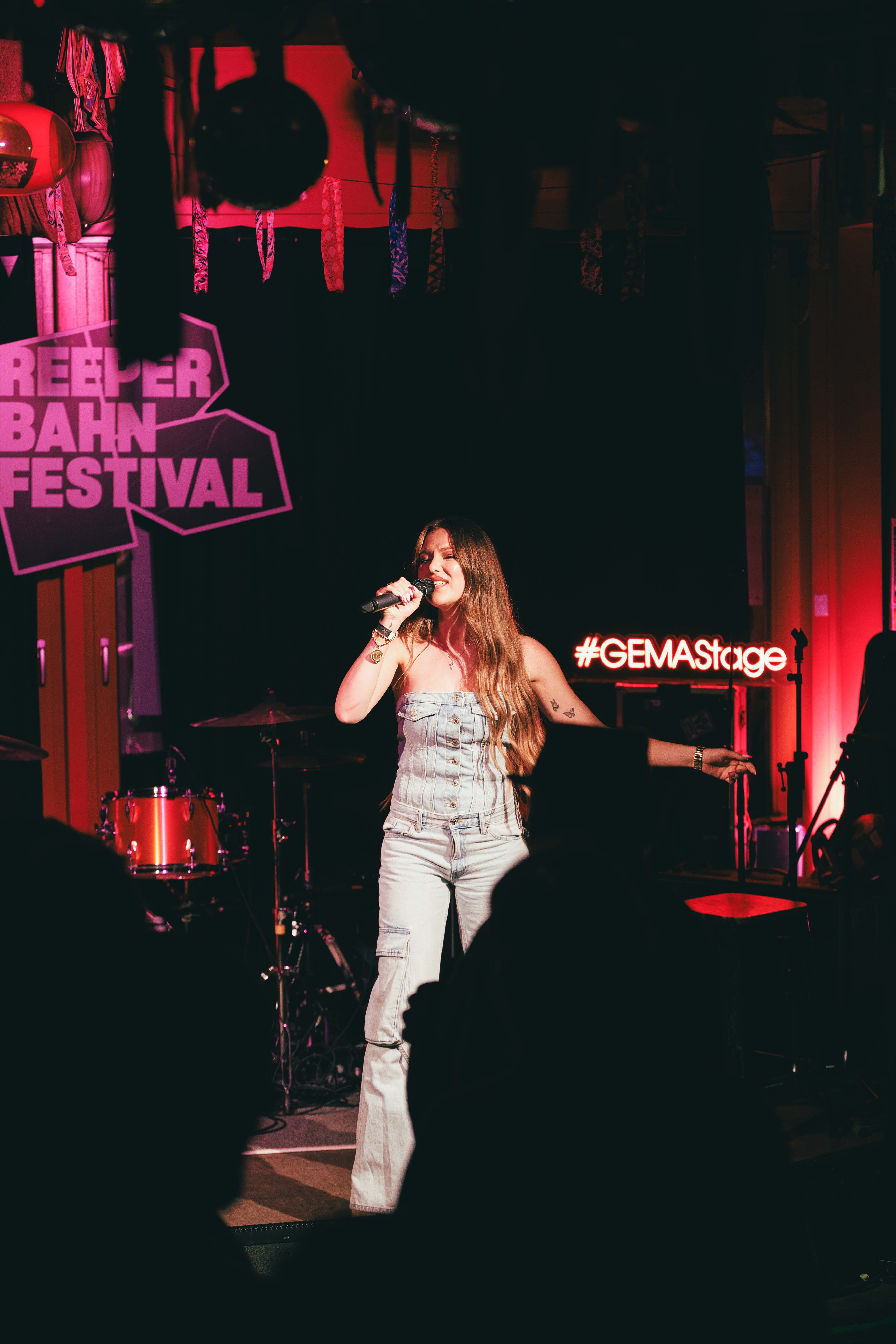Eine Frau singt auf einer Bühne beim Reeperbahn Festival, umgeben von rotem Licht und Schlagzeug.