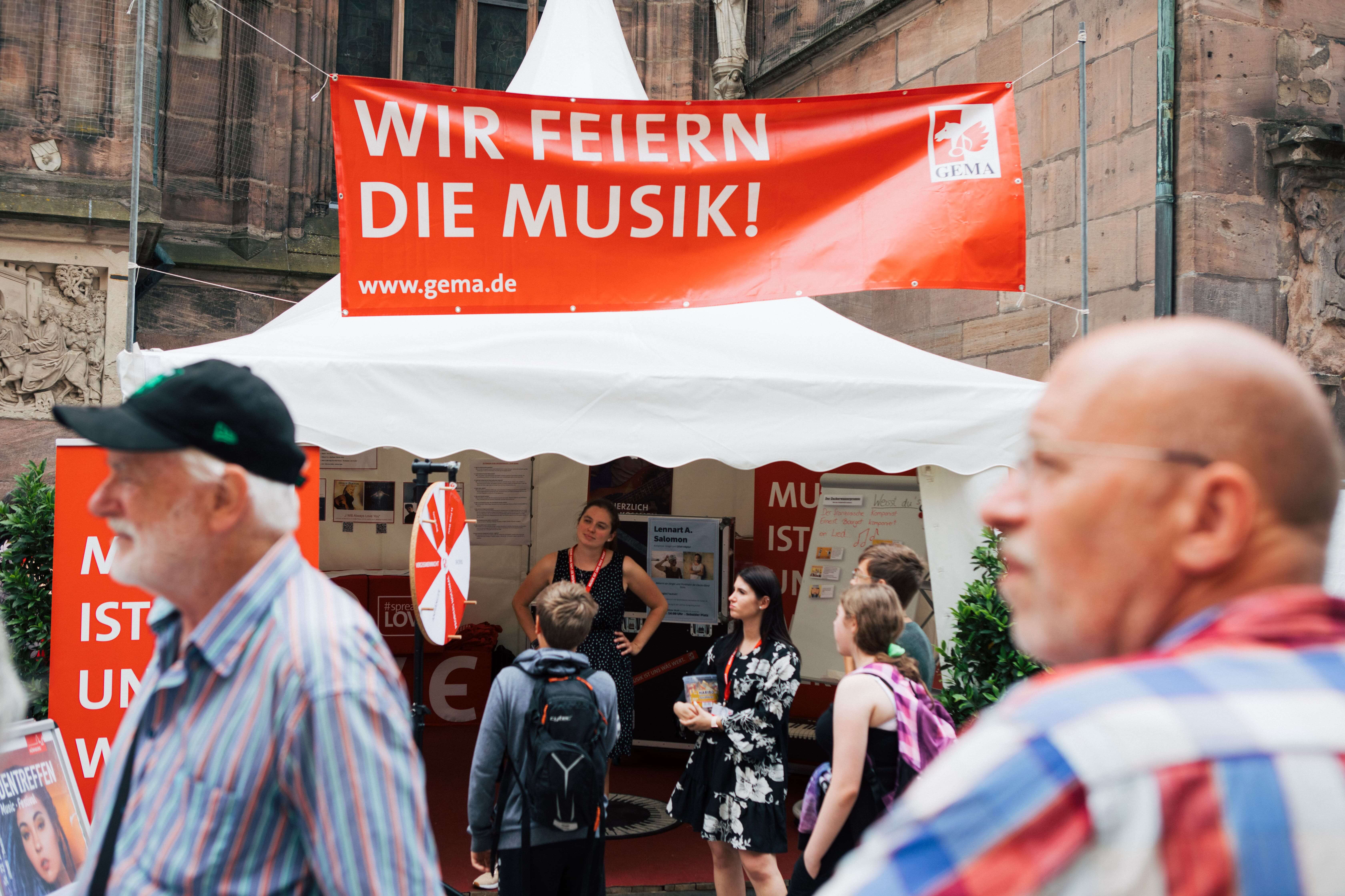 Ein rotes Banner über einem weißen Zelt mit Menschen davor auf einem Musikfestival.