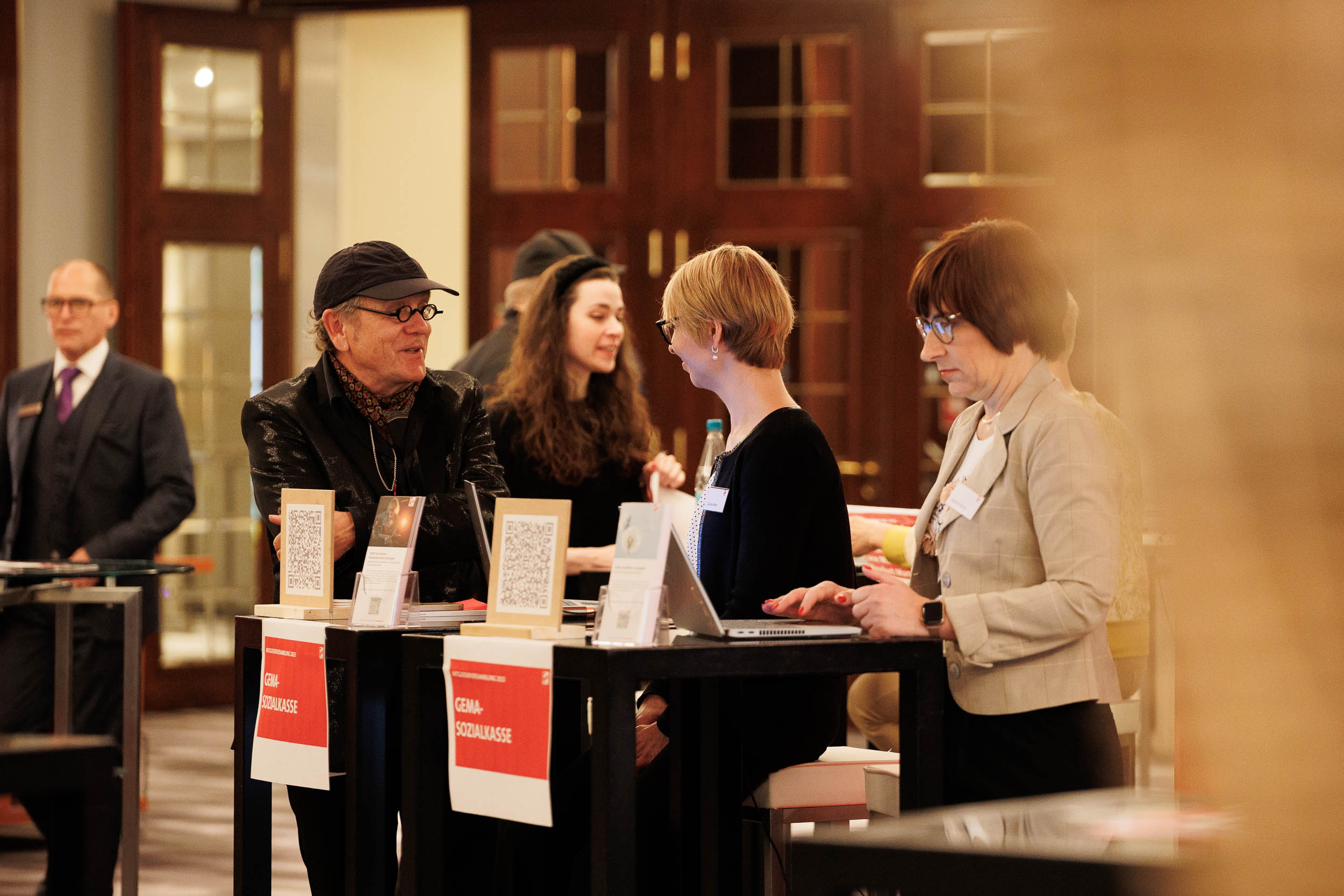 People at a conference table with laptops and QR codes, engaging in conversation, in a warmly lit room.