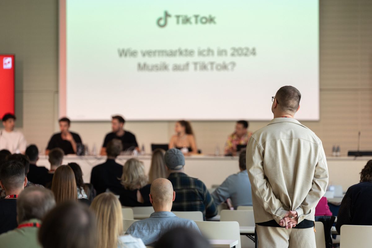 Audience watches a panel discussion on marketing music on TikTok in 2024, with a presentation screen in the background.