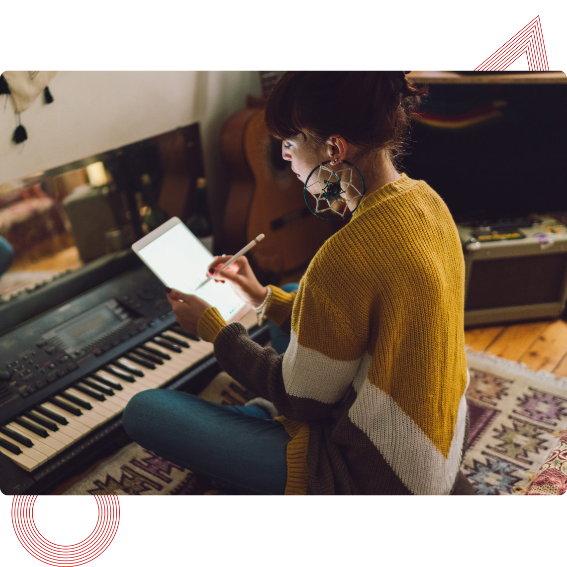 Woman in a cozy sweater writes on a tablet next to a keyboard piano, with a guitar in the background.