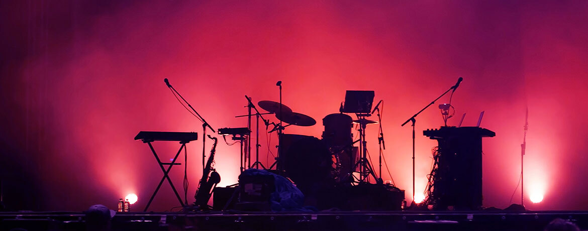 Silhouetted band setup with drums, keyboards, and microphones against a vibrant red and purple lit background.