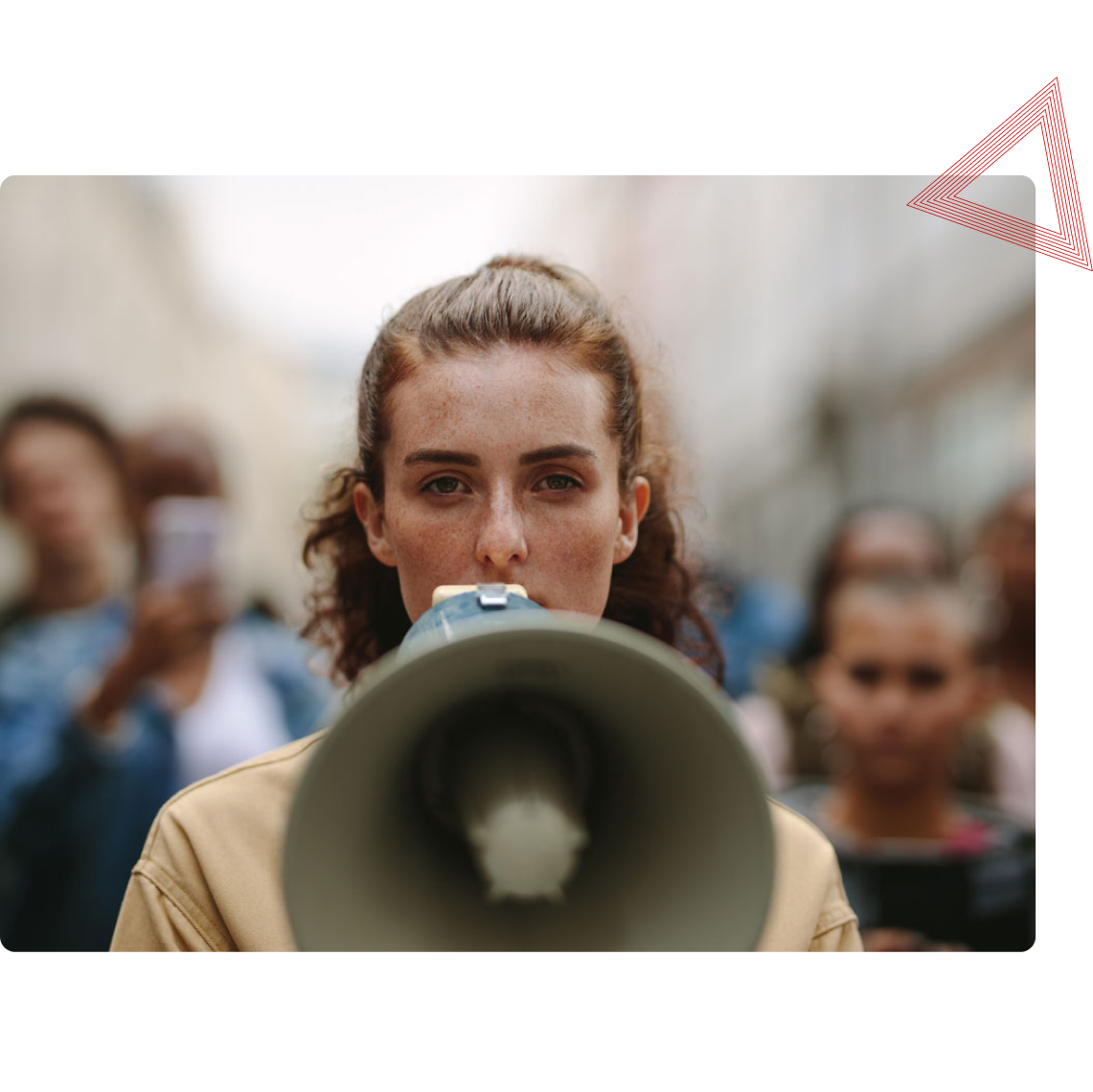 A person speaks into a megaphone in a crowd, with blurred figures in the background.