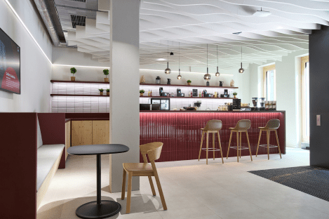 Modern cafe interior with a red counter, hanging lights, wooden stools, and a small round table with chairs.