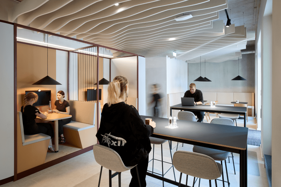 People work and converse in a modern office with wavy ceiling, booths, and black tables.