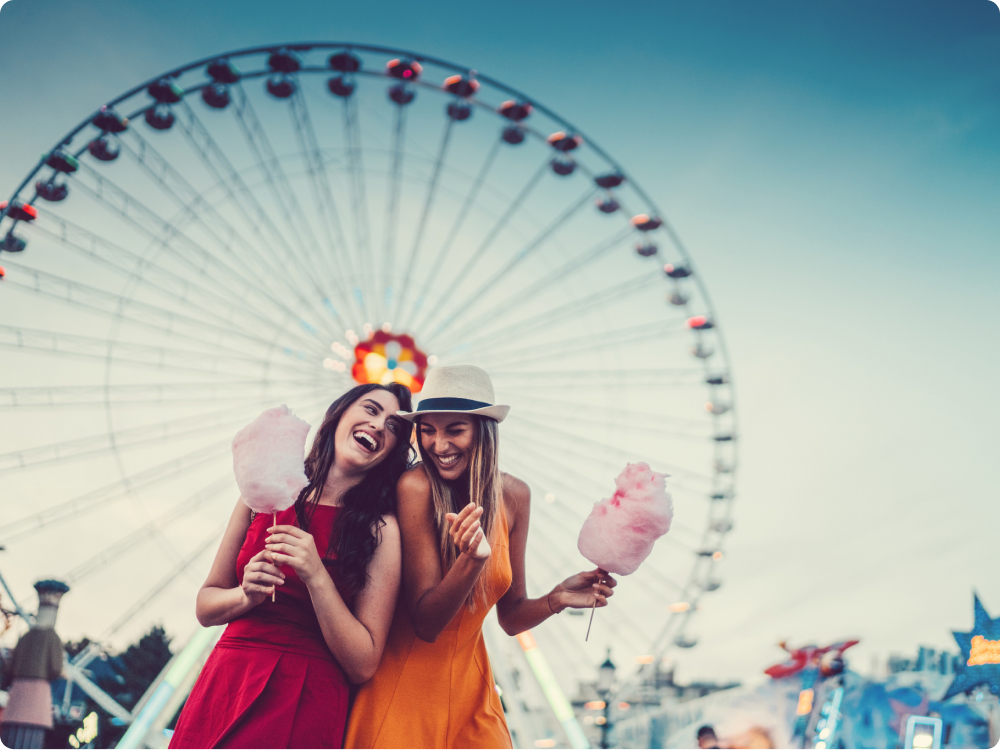 Zwei Frauen vor einem Riesenrad halten Zuckerwatte.