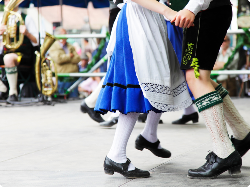 Tanzende Personen in traditioneller Tracht mit blauem Rock, weißer Schürze und schwarzen Schuhen
