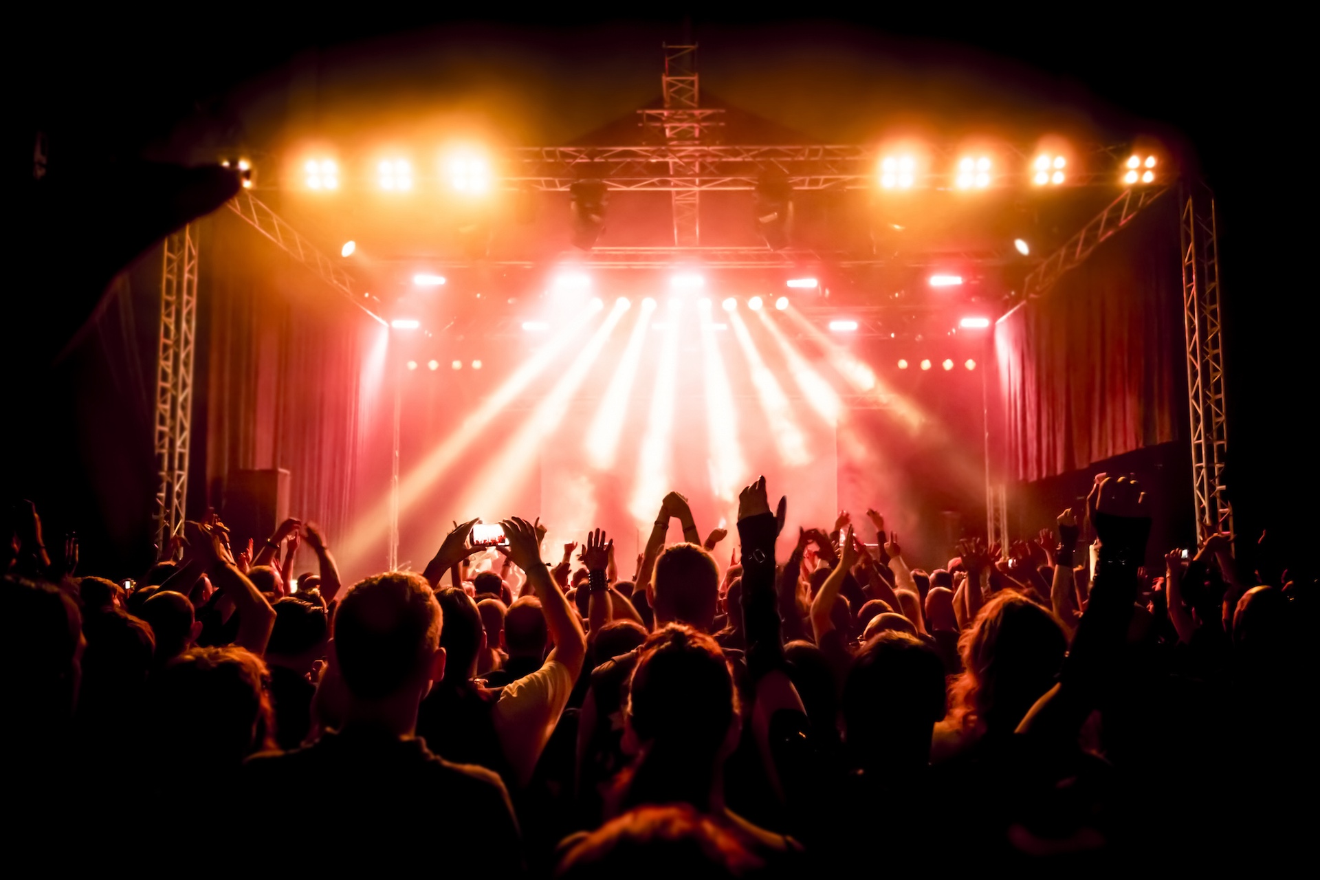 Publikum vor einer Bühne mit hellen Scheinwerfern bei einem Konzert am Abend.