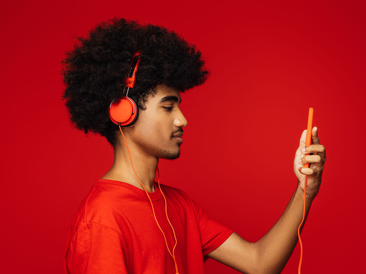 Person mit Afro trägt rote Kopfhörer und hält ein Smartphone vor rotem Hintergrund.