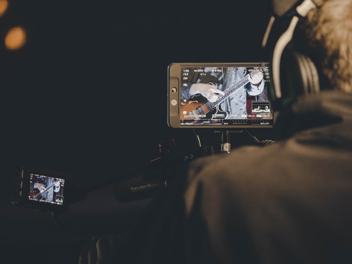 Person filming a guitarist on a camera screen in a dark setting.