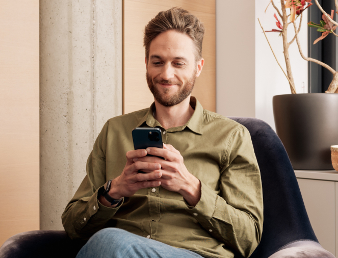 Mann in grünem Hemd sitzt lächelnd auf Sessel und schaut auf Smartphone.