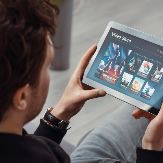 A person holds a tablet displaying a video store app with various movie thumbnails.