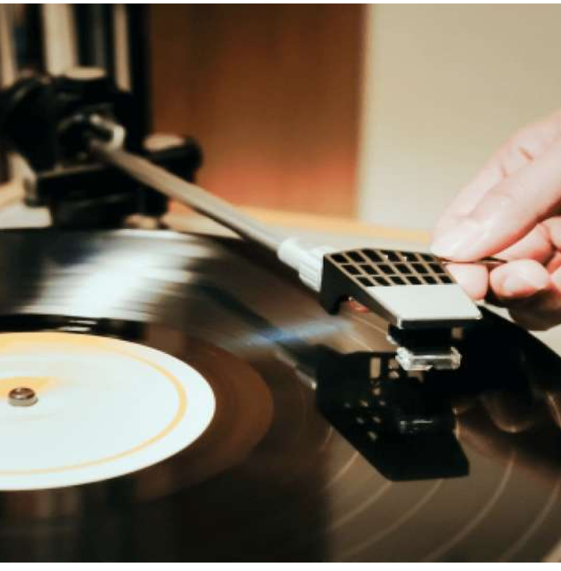 A hand places a needle on a spinning vinyl record on a turntable.