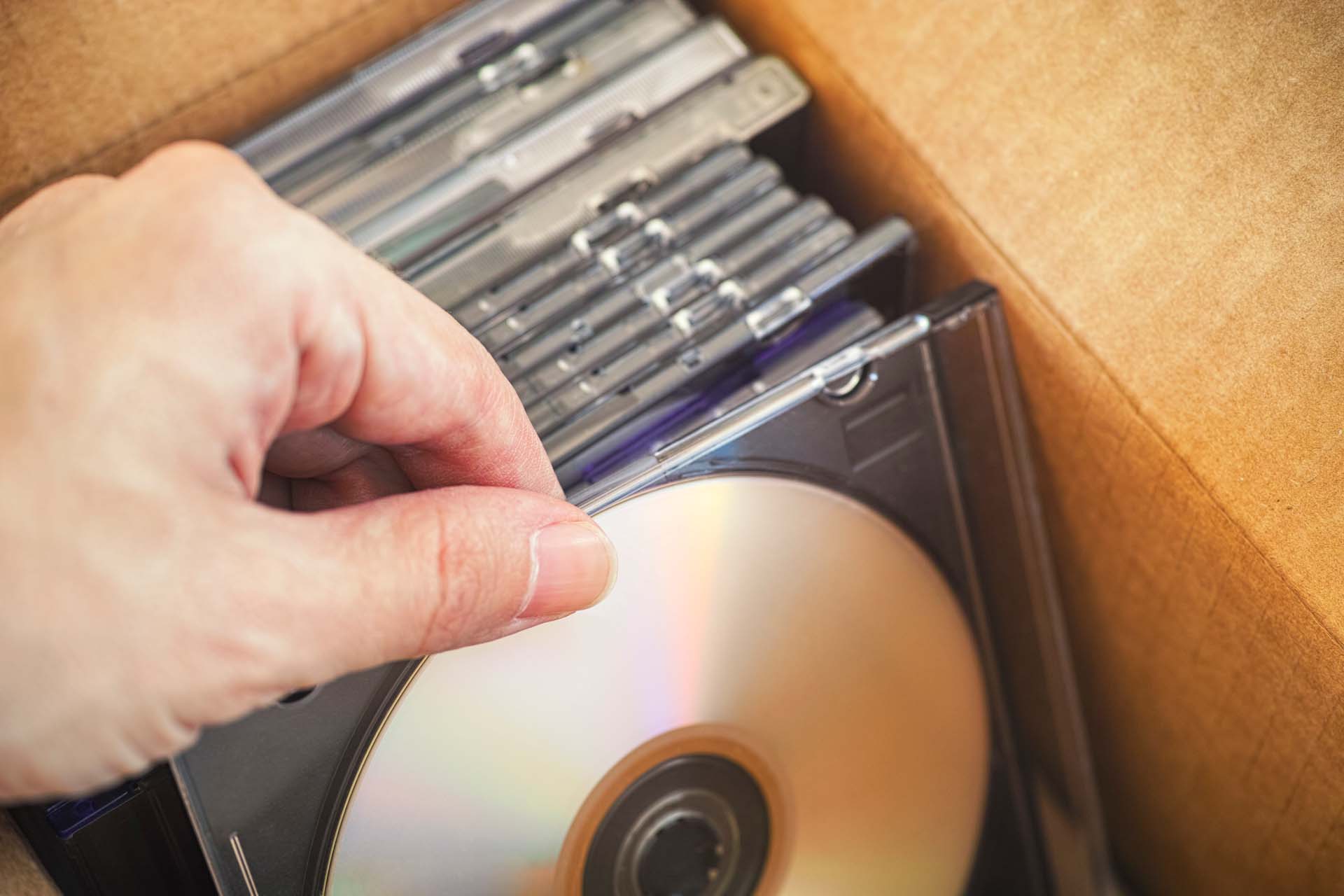 Hand greift nach einer CD in einer Pappschachtel voller CD-Hüllen.