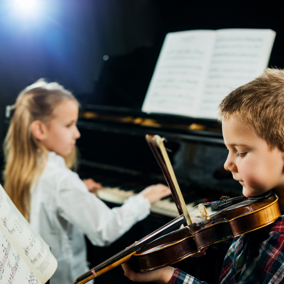 Ein Junge spielt Geige, während ein Mädchen Klavier spielt, beide vor Notenblättern.