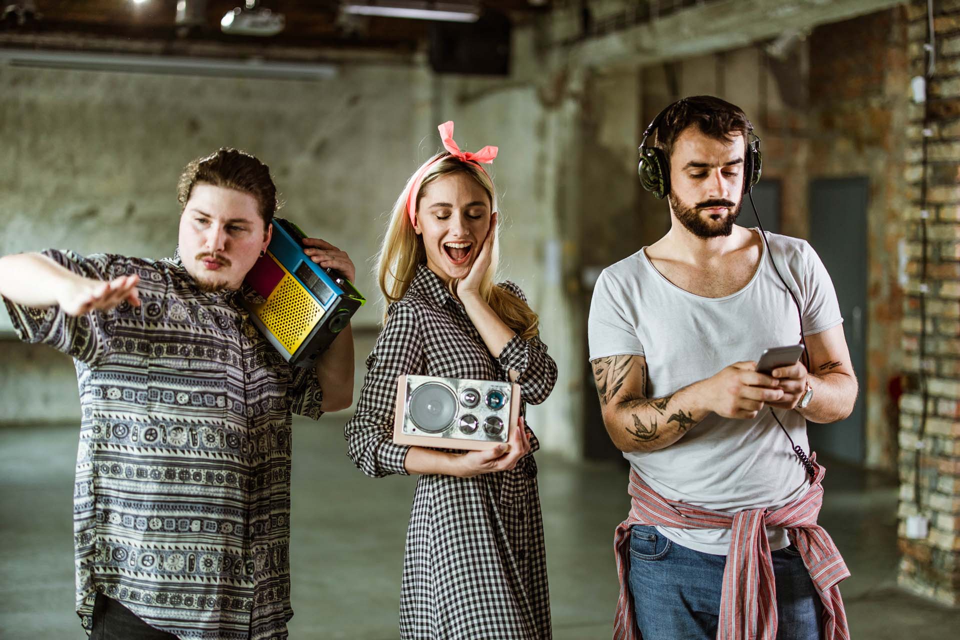 Three people enjoying music: one with a boombox, another with a radio, and the third with headphones and a phone.