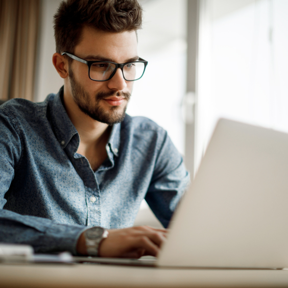 Ein Mann mit Brille arbeitet konzentriert an einem Laptop in einem hellen Raum.