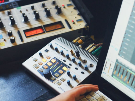 A hand on a keyboard near audio mixing equipment and a computer screen displaying sound levels.