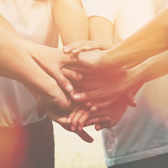 Multiple hands stacked together in a gesture of unity and teamwork, with soft lighting and a warm tone.
