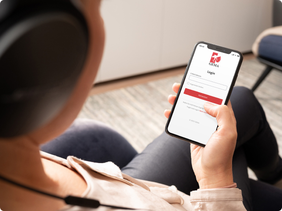 Person wearing headphones holds a smartphone displaying a login screen in a cozy room.
