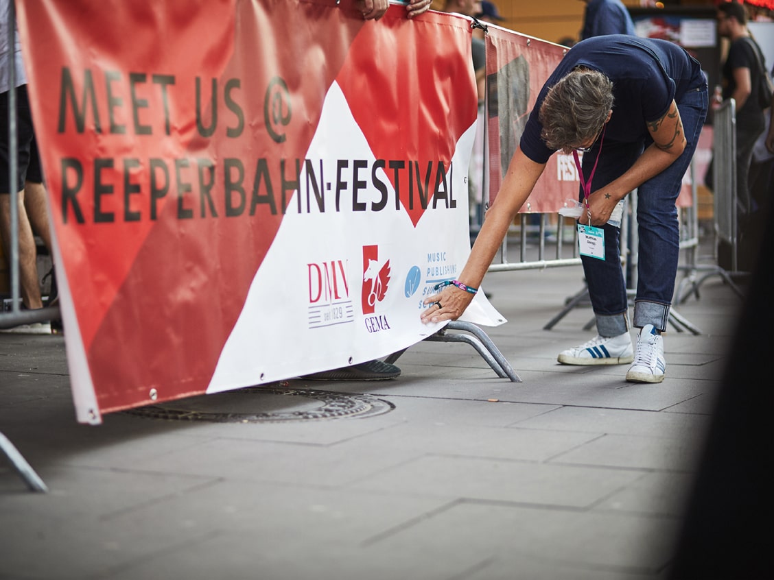 Person adjusts a red and white Reeperbahn Festival banner on a metal barrier at an outdoor event.