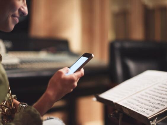 Person holding a smartphone, seated near a music stand with sheet music in a studio setting.