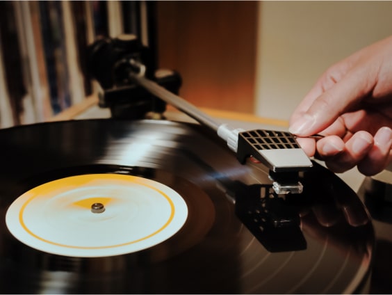 A hand places a needle on a spinning vinyl record with a white label on a turntable.
