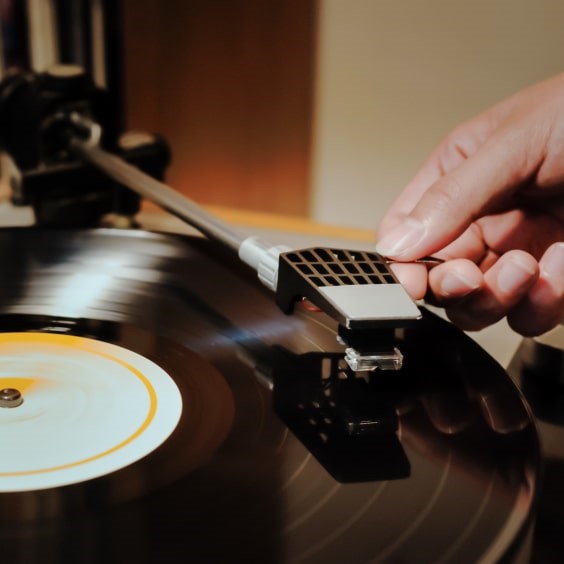 A hand adjusts the tonearm on a spinning vinyl record with a white and yellow label.