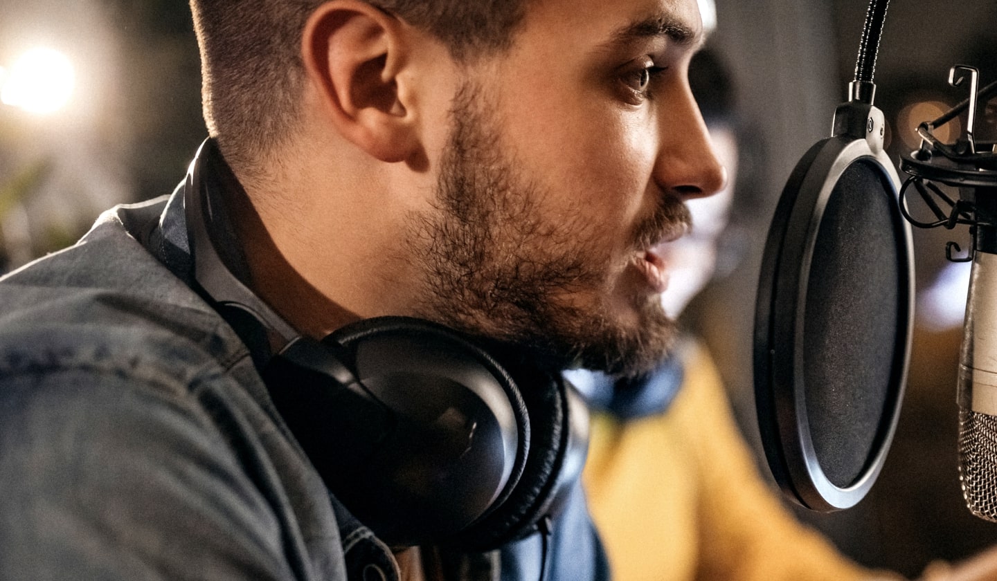 A man with headphones speaks into a microphone in a dimly lit room.