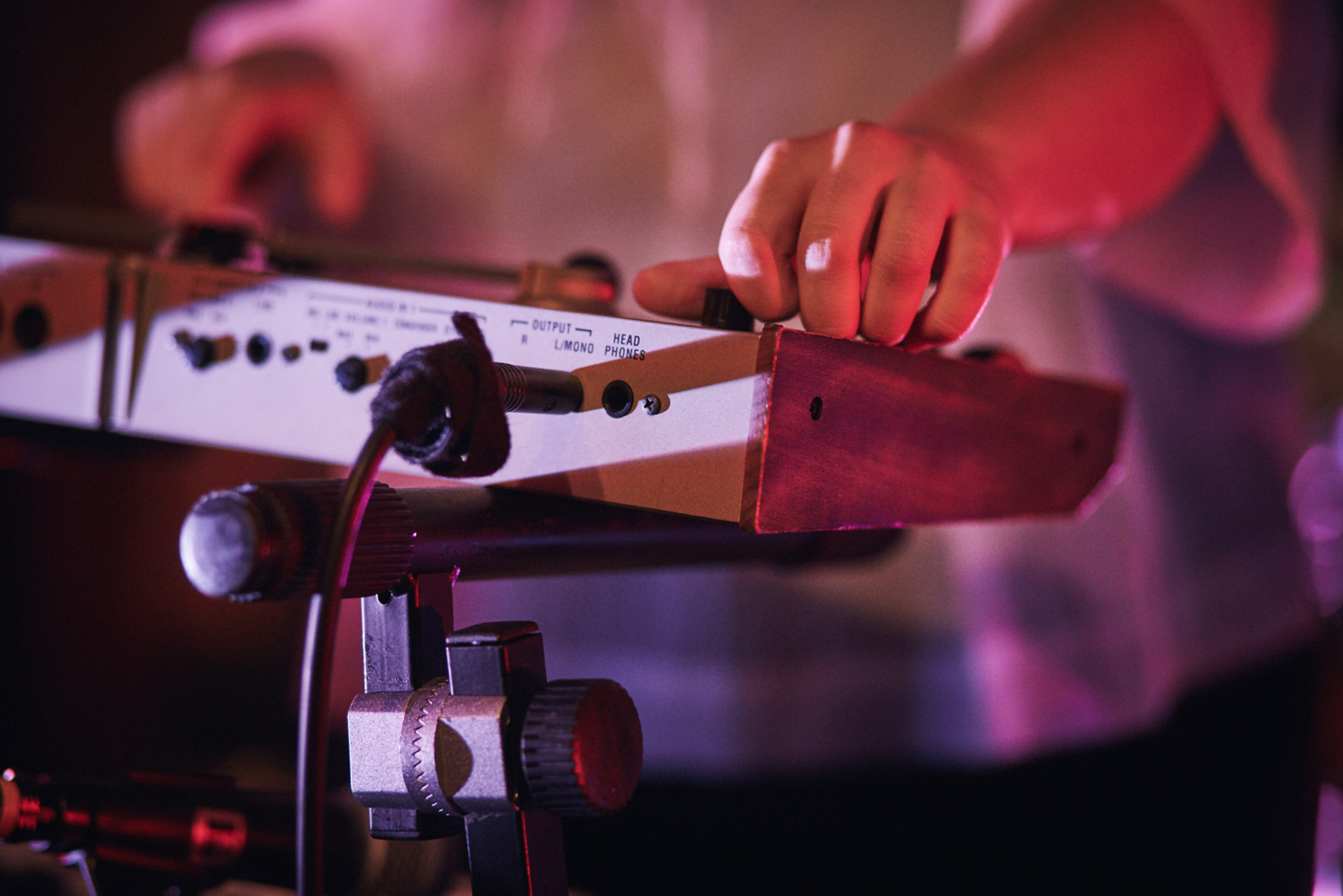 Hands adjusting knobs on a synthesizer with wooden sides, under pink lighting.