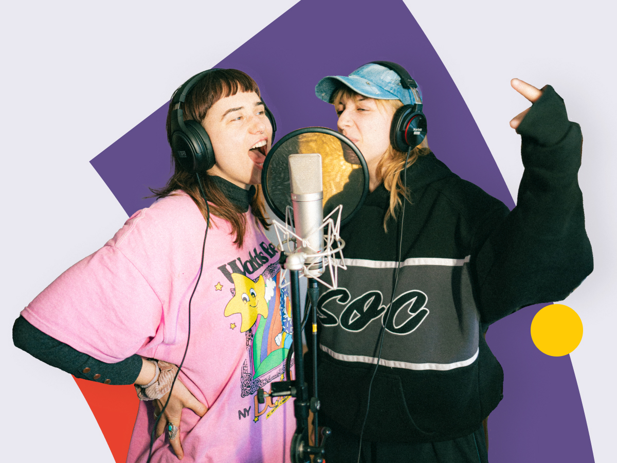 Two people sing into a microphone, wearing headphones