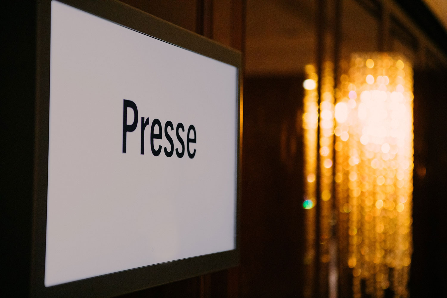 Ein Schild mit der Aufschrift 'Presse' vor einem unscharfen, goldenen Hintergrund.