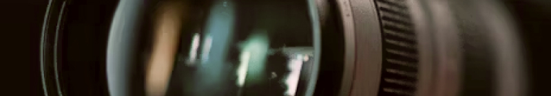 Close-up of a camera lens with reflections, set against a dark background.