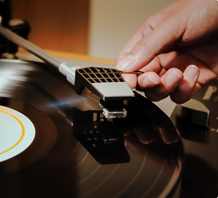 A hand places a needle on a spinning vinyl record on a turntable.
