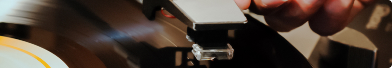 A hand places a needle on a spinning vinyl record on a turntable.