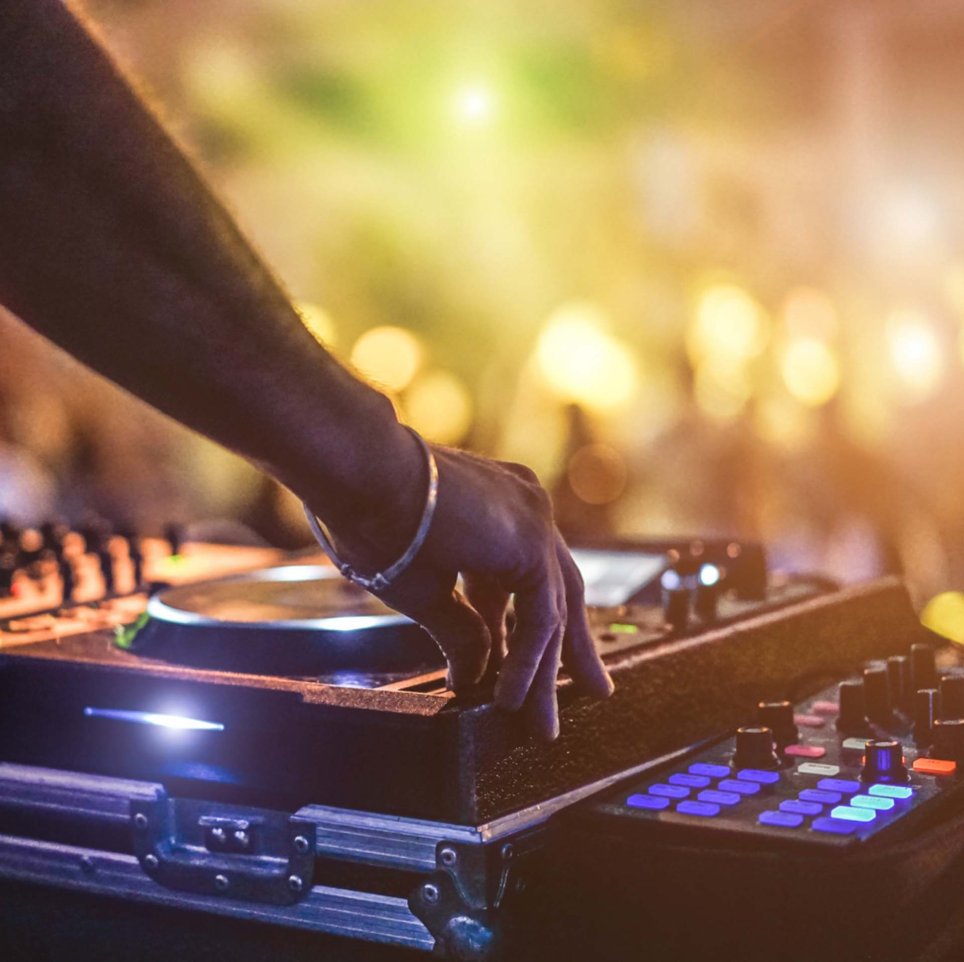 Ein DJ mixt Musik an einem beleuchteten Mischpult, umgeben von verschwommenen Lichtern im Hintergrund.