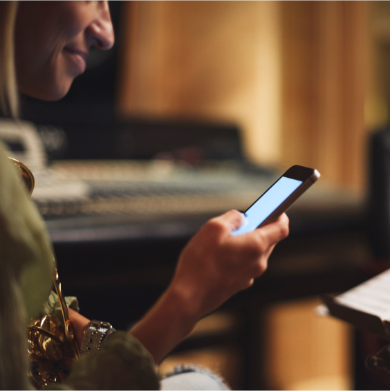 A person smiles while looking at a smartphone in a dimly lit room with music equipment.