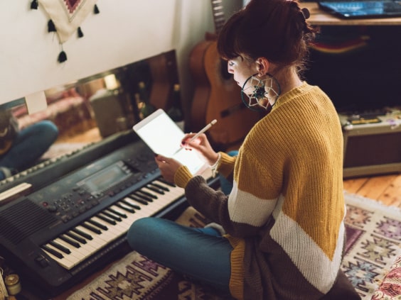 Eine Frau sitzt am Keyboard und schreibt auf einem Tablet, umgeben von Gitarren.