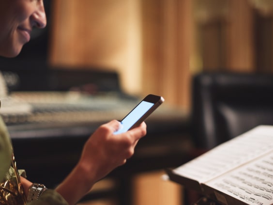 Person holding a smartphone, reading sheet music in a dimly lit room with audio equipment in the background.