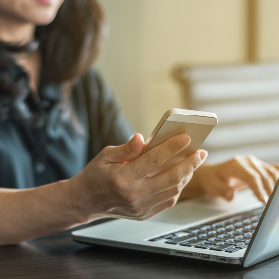 A person in a black shirt uses a smartphone and a laptop at a table.