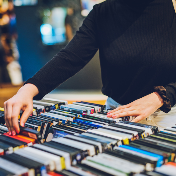 Person browsing through rows of colorful cassette tapes on a table.