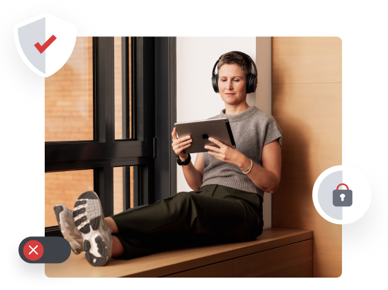 Person wearing headphones, sitting by a window, using a tablet. Feet are propped up on a bench.