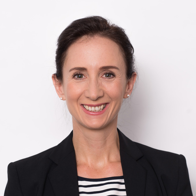Smiling woman with dark hair in a bun, wearing a black blazer and striped shirt, against a plain white background.