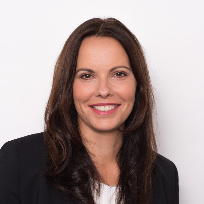 Smiling woman with long brown hair in a black blazer against a plain white background.